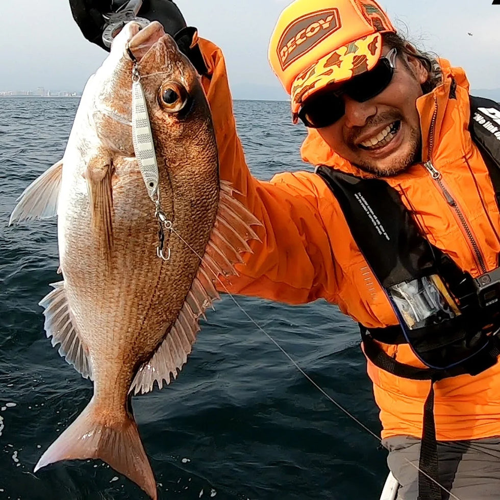 Angler in Decoy cap and vest holding a snapper caught on a jig